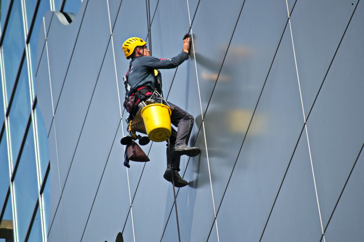 A man in safety gear ascends the side of a building, performing window cleaning services with precision and care.