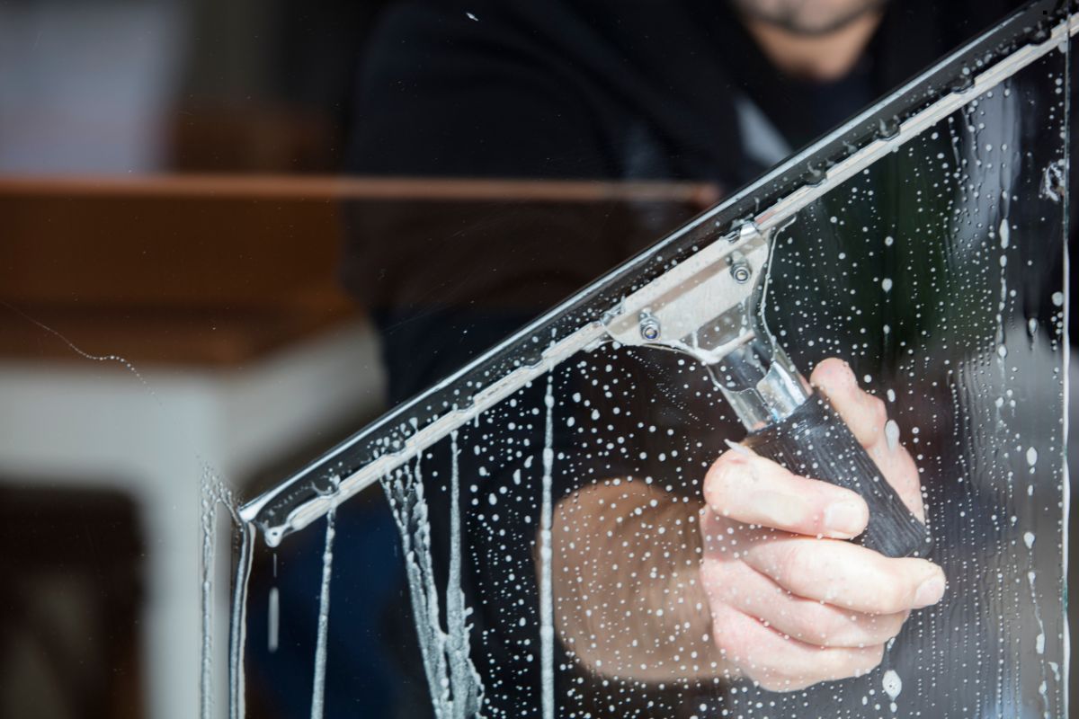 A man using a squeegee to clean a window, representing a professional window cleaning service.