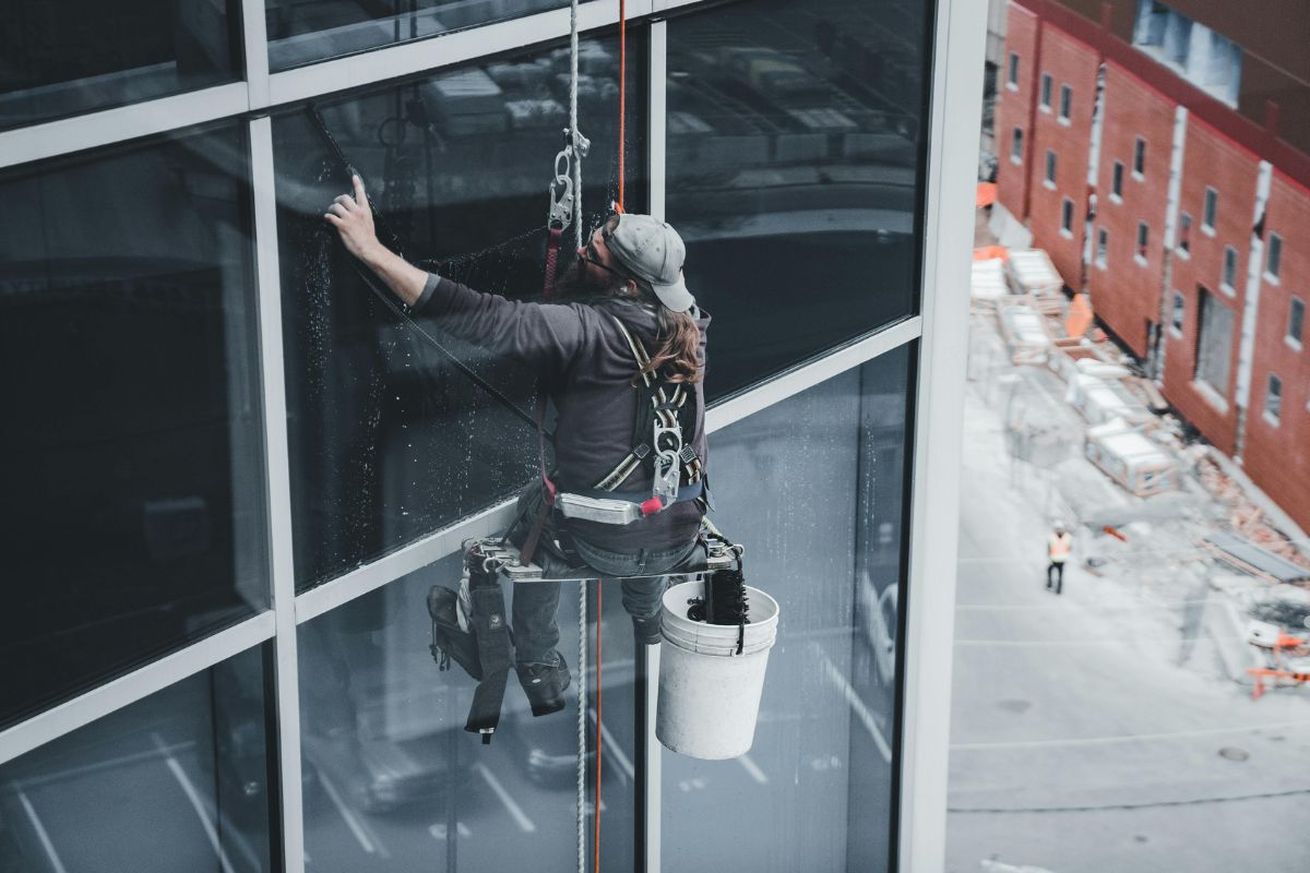 A man cleaning windows while suspended from a building on a window washer platform.