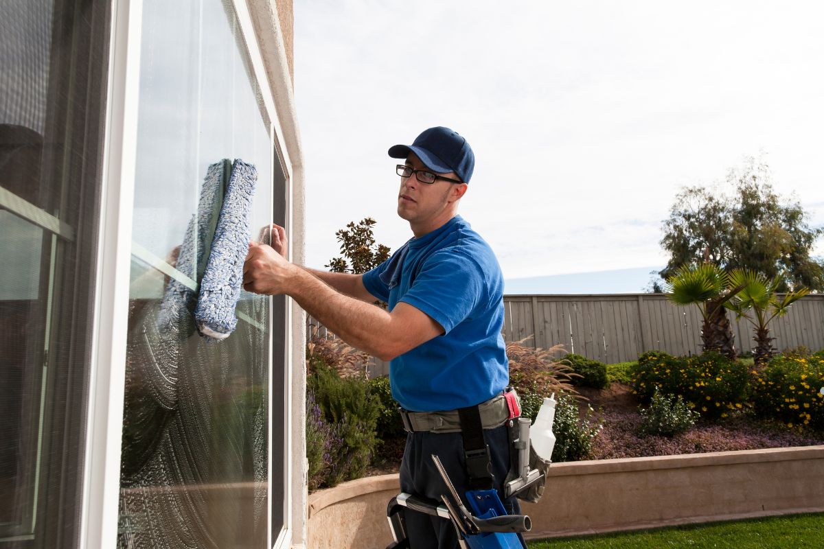A man wearing a blue shirt cleans windows using a squeegee, demonstrating effective window cleaning techniques.